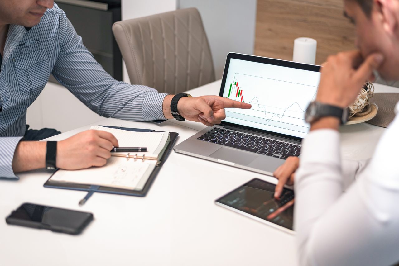 why-choose-us Two businessmen analyzing financial charts and data on a laptop and tablet.