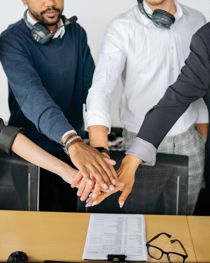 The Art of Drawing Readers In: Your attractive post title goes here Diverse colleagues joining hands on conference table, symbolizing teamwork and unity.